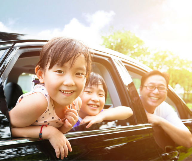 Kids and dad hanging out the car window and smiling at the camera