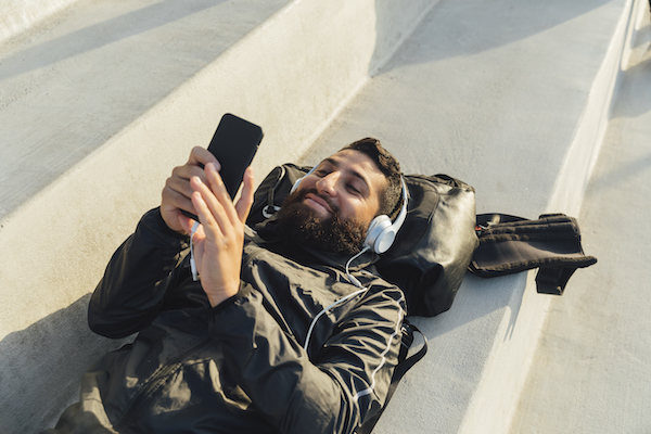 Persona en Telefono Hombre acostado en un banco mirando el telefono y escuchando musica